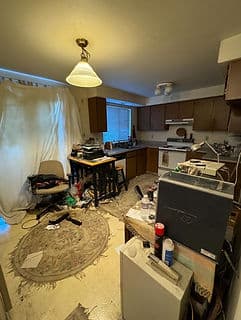 Cluttered kitchen with disorganized furniture and appliances in poor condition.