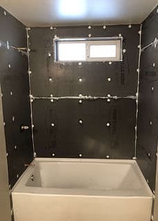 Bathroom renovation featuring bathtub and black wall board installation with window.