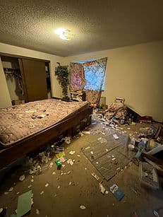 Messy bedroom with disorganized furniture, cluttered floor, and unmade bed.