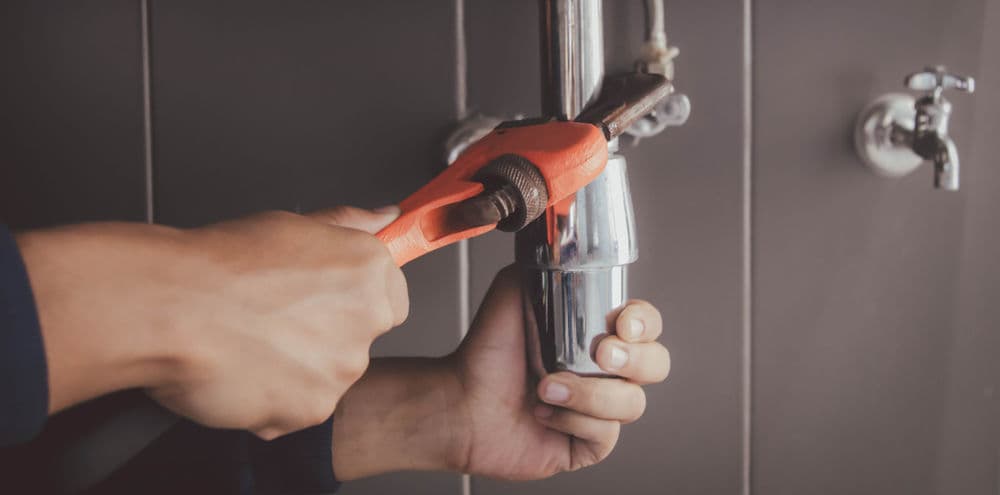 Person using an adjustable wrench to fix plumbing under a sink.